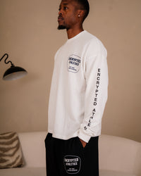 Man wearing a white long-sleeve shirt and black pants with 'Encrypted Athletics' branding in a room.